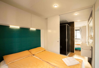 Chambre moderne avec lit double, draps jaunes et salle de bain attenante, Next XL Panorama, Chianti Glamping Resort.