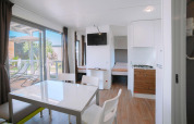Hébergement de glamping moderne et lumineux avec coin repas, kitchenette, chambre et terrasse avec transats.
