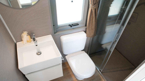 Salle de bain de glamping moderne avec toilettes, lavabo et douche vitrée près d'une fenêtre.