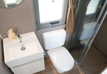 Baño moderno de glamping con inodoro, lavabo y ducha con mampara de cristal junto a la ventana.