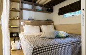 Chambre de la lodge Cottage Clever avec lit double, étagères intégrées, fenêtre et draps à carreaux.