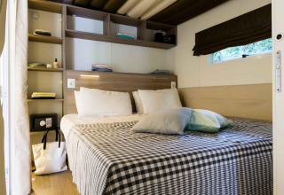Soveværelse på Cottage Clever lodge med dobbeltseng, hylder, vindue og ternet sengetøj.