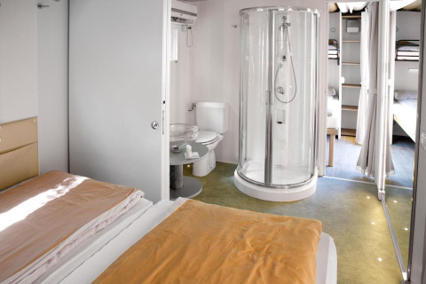 Moderne logehytte Cottage Clever med dobbeltseng, bruser, toilet og køjesenge i separat område.