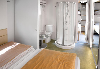 Habitación moderna en Cottage Clever con cama doble, cabina de ducha, inodoro y zona de literas visible.