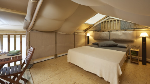 Knusse slaapkamer in Airlodge 2.0 met tweepersoonsbed, houten stoelen en zachte verlichting in tent.