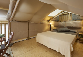 Knusse slaapkamer in Airlodge 2.0 met tweepersoonsbed, houten stoelen en zachte verlichting in tent.