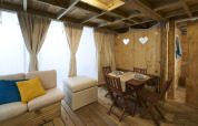 Living area in Airlodge 2.0 featuring wood decor, dining space, sofa with colored pillows, and large curtains.