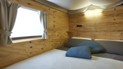 Gezellige slaapkamer met houten wand, raam en grijze lakens in Airlodge 2.0, een uniek verblijf.