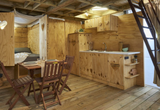 Interieur van Airlodge 2.0 met houten vloer, compacte keuken, eethoek en ladder naar de slaapzolder.
