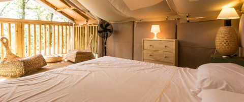Interior of Airlodge 1 at Chianti Glamping Resort, Italy, featuring bed, chairs, dresser, and balcony.