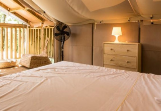Interior of Airlodge 1 at Chianti Glamping Resort, Italy, featuring bed, chairs, dresser, and balcony.