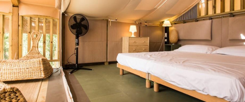 Bedroom with double bed, wooden furniture, lamps, and fan at Airlodge 1, Chianti Glamping Resort, Italy.