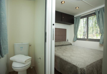 Dormitorio y baño pequeño dentro de una cabaña Cottage Next en Chianti Glamping Resort, Italia, con vista al bosque.