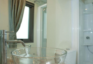 Modernes Badezimmer mit Glaswaschbecken und Spiegel im Cottage Next im Chianti Glamping Resort, Italien.