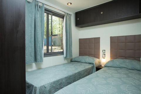 Zimmer mit zwei Einzelbetten, modernen Kopfteilen und großem Fenster im Cottage Next, Chianti Glamping Resort, Italien.