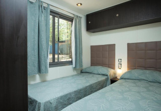 Zimmer mit zwei Einzelbetten, modernen Kopfteilen und großem Fenster im Cottage Next, Chianti Glamping Resort, Italien.