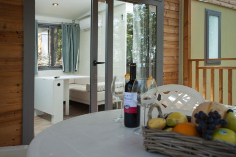 Terrasse mit Esstisch, Weinflasche, Gläsern und Obstkorb am Cottage Next im Chianti Glamping Resort, Italien.