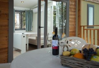 Terrasse mit Esstisch, Weinflasche, Gläsern und Obstkorb am Cottage Next im Chianti Glamping Resort, Italien.