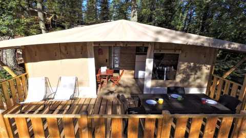 Terrazza esterna con tavolo da pranzo, sedie e sdraio davanti a una lodge tent al Chianti Glamping Resort, Italia.