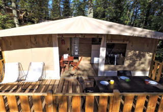 Terrazza esterna con tavolo da pranzo, sedie e sdraio davanti a una lodge tent al Chianti Glamping Resort, Italia.