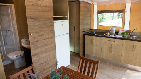 Indvendigt vue af Lodge Tent Deluxe glamping med køkken, spisebord, badeværelse og vindue til naturen.