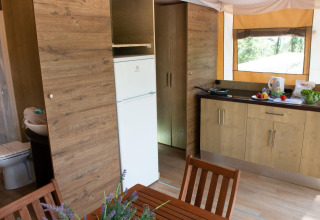 Indvendigt vue af Lodge Tent Deluxe glamping med køkken, spisebord, badeværelse og vindue til naturen.