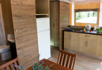Vista interna del Lodge Tent Deluxe glamping con cucina, zona pranzo, bagno e finestra sulla natura.