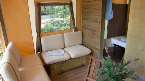 Vue intérieure du Lodge Tent Deluxe glamping avec canapés confortables, fenêtre et chambre en arrière-plan.