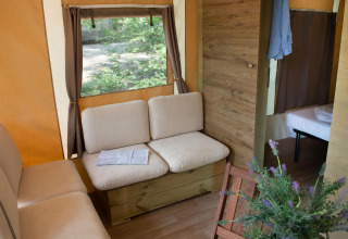 Vista interna della Lodge Tent Deluxe glamping, con divani comodi, finestra e camera da letto sullo sfondo.