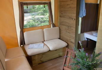 Vista interna della Lodge Tent Deluxe glamping, con divani comodi, finestra e camera da letto sullo sfondo.