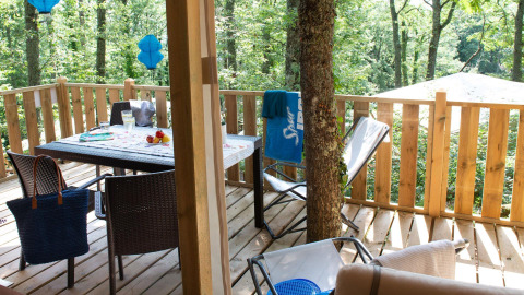 Terrasse en bois Lodge Tent Deluxe glamping avec table, chaises et vue sur la forêt verdoyante.