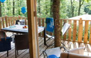Terrasse en bois Lodge Tent Deluxe glamping avec table, chaises et vue sur la forêt verdoyante.
