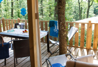 Terrasse en bois Lodge Tent Deluxe glamping avec table, chaises et vue sur la forêt verdoyante.