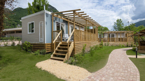 Chalet 'Next XL Superior Dog' bij Lago Idro Glamping Boutique in Italië met houten terras en groene tuin.