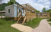 Chalet 'Next XL Superior Dog' bij Lago Idro Glamping Boutique in Italië met houten terras en groene tuin.