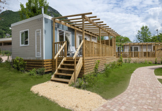 Chalet 'Next XL Superior Dog' bij Lago Idro Glamping Boutique in Italië met houten terras en groene tuin.