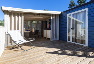Holzterrasse des Cottage Clever bei Lago Idro Glamping Boutique in Italien mit Stuhl und Überdachung.