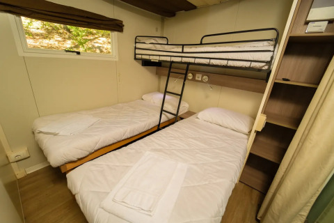 Zimmer mit Etagenbett und zwei Einzelbetten im Cottage Clever Glamping, helles Interieur und Fenster.