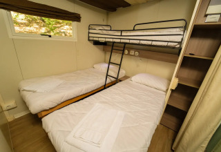Zimmer mit Etagenbett und zwei Einzelbetten im Cottage Clever Glamping, helles Interieur und Fenster.