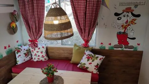 Rincón acogedor en Cottage Spotty con cortinas rojas, mural de perro, banco y cojines florales.