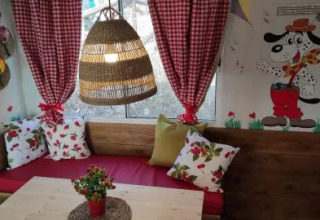 Rincón acogedor en Cottage Spotty con cortinas rojas, mural de perro, banco y cojines florales.