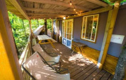 Gemütliche Holzveranda im Cottage Spotty im Chianti Glamping Resort, Italien, mit Stühlen und Lichterkette.