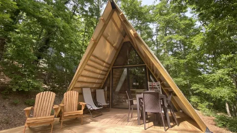 Lodge ‘A Luxury’ van Chianti Glamping Resort in Italië, houten A-frame hut met terras en stoelen in groene omgeving.