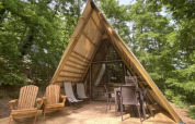Lodge „A Luxury“ im Chianti Glamping Resort in Italien, A-förmiges Holzhaus mit Terrasse und Gartenmöbeln im Wald.
