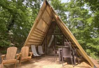 Lodge ‘A Luxury’ van Chianti Glamping Resort in Italië, houten A-frame hut met terras en stoelen in groene omgeving.