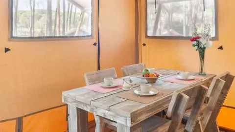 Binnenaanzicht van een safaritent in Chianti Glamping Resort Italië, met houten eettafel en vier stoelen.