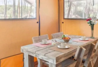 Inside a safari tent at Chianti Glamping Resort, Italy, with a rustic wooden dining table set for four guests.