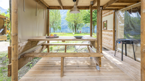 Zona de comedor exterior en la tienda safari 'Air Dreamer' en Lago Idro Glamping Boutique, Italia, con bancos de madera.
