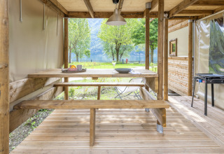 Zona de comedor exterior en la tienda safari 'Air Dreamer' en Lago Idro Glamping Boutique, Italia, con bancos de madera.