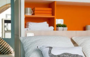 Modernes Zeltinterieur mit orangener Wand, weißen Handtüchern und Deko im Chianti Glamping Resort Italien.